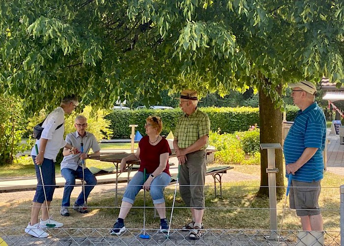 Mehrere VMCler plaudern im Schatten und beobachten die anderen beim Minigolf spielen